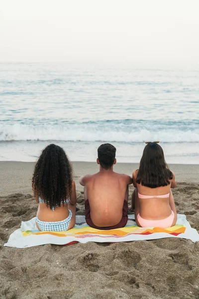 Amigos sentados en la costa mirando las olas — Foto de Stock
