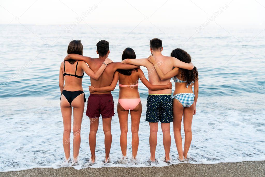 Young friends embracing on foamy seaside