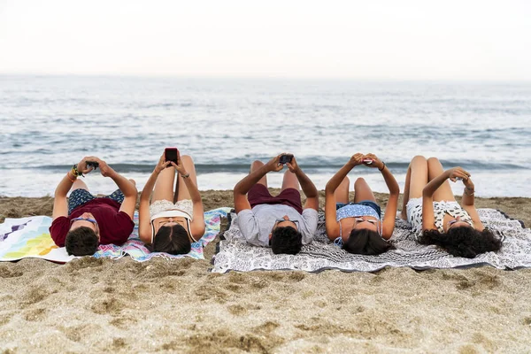 Νέοι άνθρωποι που βρίσκονται στην κουβέρτα στην παραλία και σέρφινγκ smartphones — Φωτογραφία Αρχείου