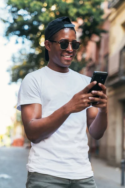 Чёрный мужчина в солнечных очках смотрит на смартфон — стоковое фото
