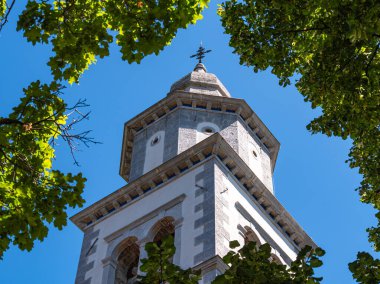 Gökyüzüne karşı yeşil yapraklarla çerçevelenmiş rüzgar gülü tarihi bir taş kule..