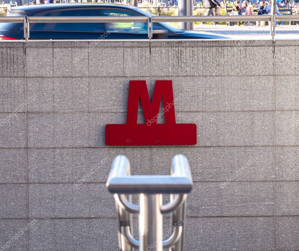 Copenhagen, Denmark - 7 September 2025: Red metro sign on a gray wall with blurred car passing above.
