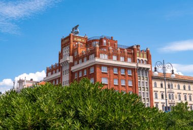 Trieste, İtalya - 1 Ağustos 2025: Yeşil ve mavi gökyüzüne sahip Generali sigorta şirketinin kırmızı tuğla binası