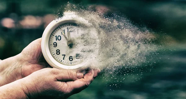 Ретро будильник в старой руке. Время бежит концепция показывает часы, которые растворяются в маленьких частицах Стоковое Изображение