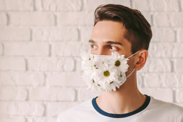 Young male doctor wearing summer medical face mask for personal protection against coronavirus and smiling. Happy man in protective face mask with daisy flowers. COVID-19 prevention. Spring allergy