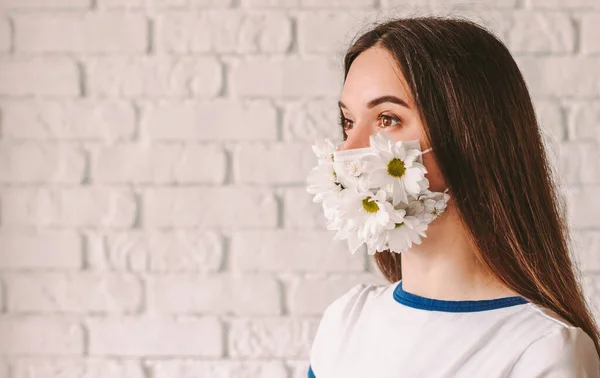 Portrait beautiful young woman doctor in medical face mask with flowers look at copy space, smile. Happy good girl wearing summer protective face mask. Coronavirus COVID-19 protection. Spring allergy