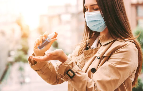 Happy girl medical face mask apply antiseptic gel on hand on city street. Beautiful stylish hipster woman in protective face mask using antibacterial sanitizer on palm outdoors. Hygiene, safety