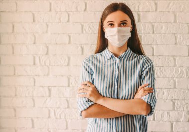 Young girl female doctor in protective mask on face keeping arms crossed in hospital. Confident sick woman in medical face mask at home quarantine. Personal protection. Coronavirus COVID-19 prevention clipart