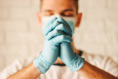 Tıbbi maskeli ve koruyucu eldivenli dindar katolik doktor hastanede Tanrı 'ya dua ediyor. Genç Hıristiyan dua eden tıbbi eldivenler ve kilisede koruyucu yüz maskesi. COVID-19 coronavirüs yardımı