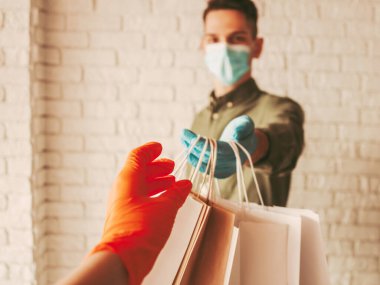 Koruyucu maske ve tıbbi eldiven takan kurye müşteriye kese kağıdı veriyor. Kağıt paketler alan bir kız. Süpermarketten eve güvenli bir teslimat. COVID-19 Coronavirüs