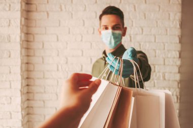 Çevrimiçi dağıtım servisinden kağıt paketleri alan bir kız. Tıbbi maskeli kurye ve koruyucu eldivenli kurye müşteriye kağıt alışveriş torbaları veriyor. Güvenli teslimat, Coronavirus COVID-19