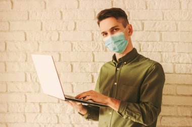 Tıbbi maskeli bir iş adamı evde dizüstü bilgisayarla çalışıyor. Hipster öğrenci mesafesi çalışması bilgisayarda. Çevrimiçi mağazadan koruyucu maskeli bir adam. Coronavirus COVID-19 karantina, uzak iş