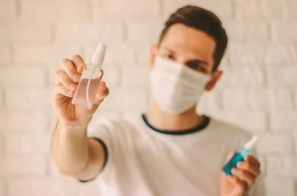 Confident man in medical face mask holding antibacterial gel bottles in hands. Young professional doctor in protective mask on face showing sanitizers. Personal safety, hygiene. Coronavirus COVID-19
