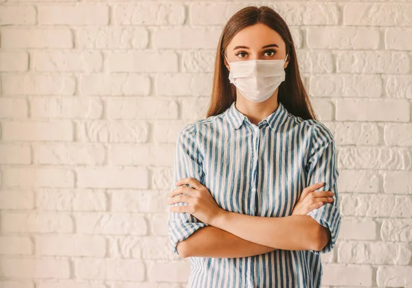 Koruyucu maskeli genç bayan doktor hastanede kollarını kavuşturuyor. Ev karantinasında kendine güvenen hasta bir kadın var. Kişisel koruma. Coronavirus COVID-19 önleme