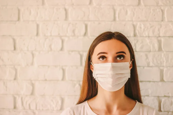 Young scared woman in medical mask on face looking up at copy space. Confident female doctor in protective face mask in hospital. Girl medic in face mask. Coronavirus COVID-19 personal protection