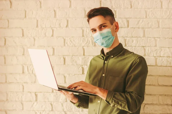 Tıbbi maskeli bir iş adamı evde dizüstü bilgisayarla çalışıyor. Hipster öğrenci mesafesi çalışması bilgisayarda. Çevrimiçi mağazadan koruyucu maskeli bir adam. Coronavirus COVID-19 karantina, uzak iş