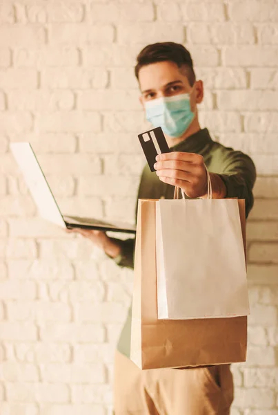 Junger Mann Mit Mundschutz Kreditkarte Laptop Und Einkaufstaschen Der Hand — Stockfoto