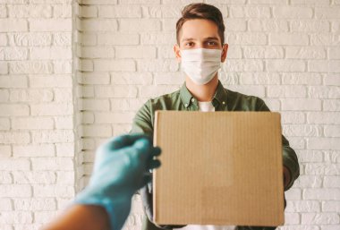 Plastik koruyucu eldivenli POV müşterisi teslimat elemanından kargo kutusu alıyor. Tıbbi maskeli mutlu hippi kurye mukavva kutuyu müşteriye ver. Güvenli karantina teslimatı