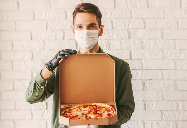 Hipster guy courier in medical face mask and gloves hold cardboard pizza box in hands. Happy man delivery service worker in protective mask carry open tasty pizza box. Italian fast food. Food delivery