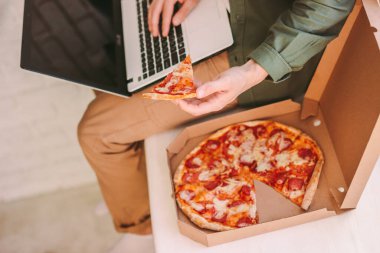 Üst düzey hippi adam dizüstü bilgisayarda klavye yazıyor, bir dilim lezzetli pizzayı tutuyor, rahat bir iş yerinde internette sörf yapıyor. Aç işadamı İtalyan yemeği yer, bilgisayarla çalışır. Uzak ofis