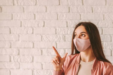 Şık, koruyucu maskeli güzel hippi kızın portresi fotokopi alanına bakıyor. Pembe tıbbi maskeli mutlu moda kadın fotokopi alanını işaret ediyor. COVID-19 karantina modası