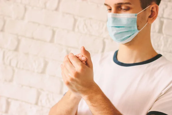Young doctor in medical mask on face rubbing hands with sanitizer. Confident man using antibacterial gel for washing hands as preventive measure against contagious disease. COVID-19, Coronavirus