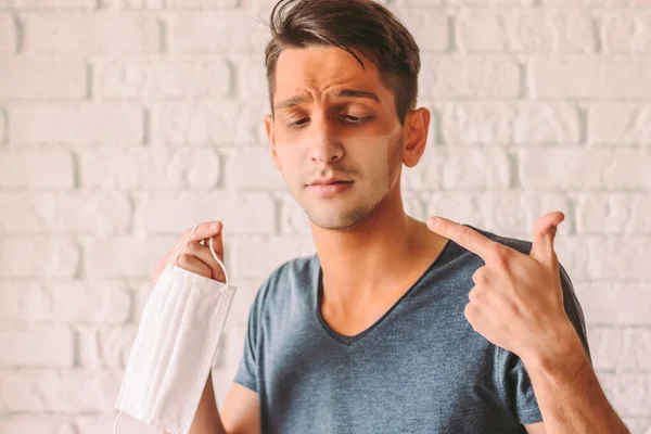 Portrait of young hipster man with red sunburn skin after wearing medical face mask. Confused man with funny sun tan lines on face from protective face mask. Preventive measures for COVID-19 patients