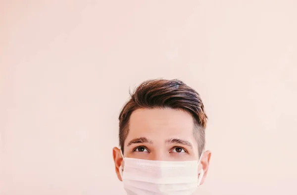 Young confident man fitness instructor in medical face mask looking up at background with copy space. Happy sports man in protective face mask. Personal protection, home quarantine training, COVID-19