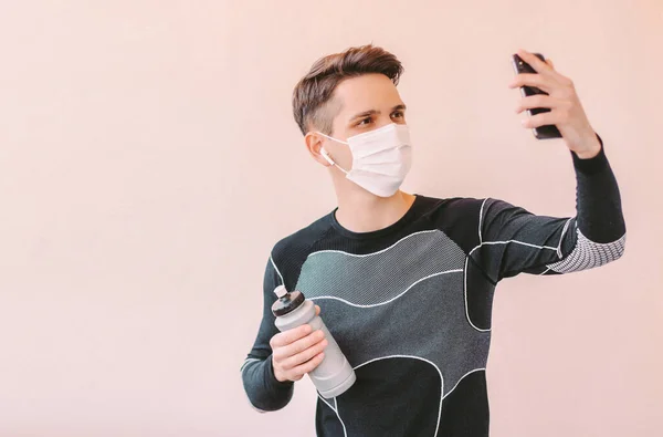 Genç adam fitness koçu, blog yazarı, tıbbi koruyucu yüz maskesi kaydeden video eğitmeni. Çevrimiçi eğitim dersinde telefonu elinde tutan mutlu sporcu. COVID-19 karantina