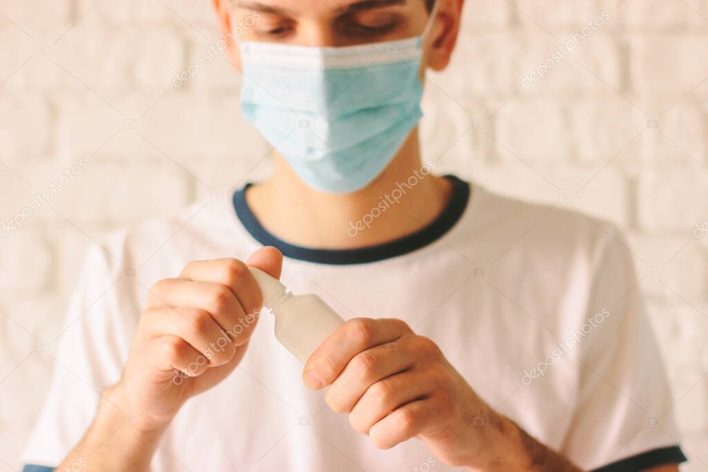 Portrait of young sick man with runny nose using nasal spray. Confident ill man doctor in medical face mask holding nose drops for congested nose. Pandemic coronavirus COVID-19, nCov-19 symptoms
