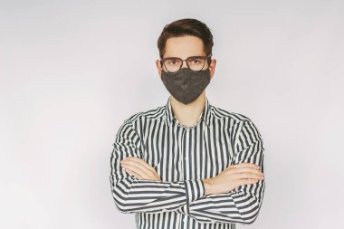 Koruyucu yüz maskeli, gözlüklü genç ve başarılı iş adamı portresi beyaz arka planda kollarını çapraz tutuyor. Kendine güvenen profesyonel girişimci şık gözlüklü, tıbbi maskeli.