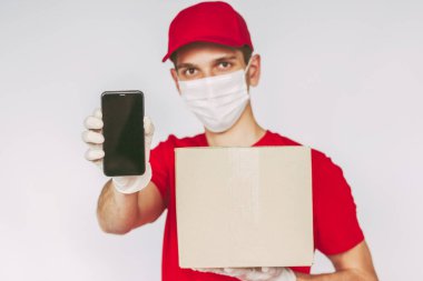 Koruyucu maske takan portre teslimatçısı, tıbbi eldiven cep telefonu taşıyan, paket kutusu elinde, izole bir geçmişi var. Adam teslimat servisi kuryesi akıllı telefon, karton kutu, boş kopya alanı