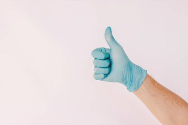 Yakından bir doktor, beyaz arka planda izole edilmiş tıbbi lateks eldivenle baş parmak işareti gösteriyor. Mavi koruyucu eldiven giymiş erkek el hareketi anlaşması tamam gibi. Tavsiye, tavsiye, tamam, COVID-19