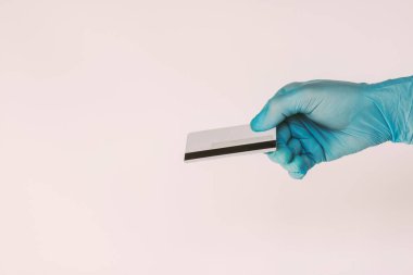 Tıbbi lateks eldivenli yakın plan adam beyaz arka planda boş kredi kartı tutuyor. Erkek el, temassız ödeme için banka kartı verir. E-ticaret, nakit para, NFC teknolojisi.