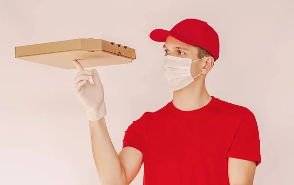 Portrait happy takeaway fast food delivery service employee spin cardboard pizza box on finger isolated on white background. Delivery guy in medical face mask and protective glove carry italian pizza