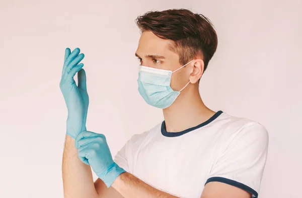 Portrait young happy male nurse in medical face mask wear protective latex gloves isolated white background. Man doctor surgeon in protective mask put on medical gloves. COVID-19 personal protection