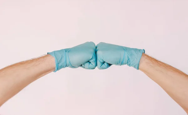 Two male doctor hands bumping hands in medical latex gloves isolated on white background. Man surgeons in blue protective gloves clapping fists. COVID-19 protection, teamwork, success, social distance