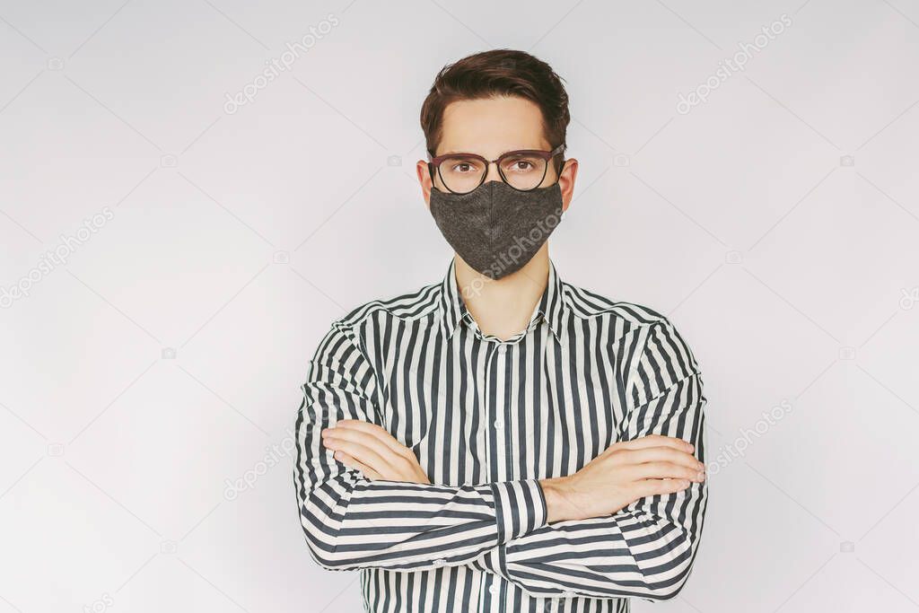 Portrait young successful businessman in protective face mask, eyeglasses keep arms crossed isolated on white background. Confident man professional entrepreneur in stylish eyewear, medical face mask