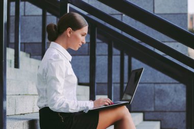 Şehir caddesinde bilgisayar klavyesi yazan kendine güvenen güzel kız öğrenci. Genç çekici iş kadını ofis binasının dışında çalışmak için dizüstü bilgisayar kullanıyor. Mutlu Milenyum Kızları Serbest Sörf İnterneti