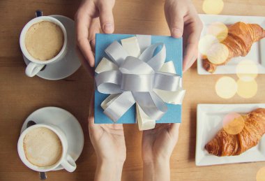 Fransız kafesinde kahve içerken sevgilisinden bayram hediyesi alan bir adamın en iyi görüntüsü. Sevgili erkek arkadaşına hediye veren kadın ellerine yakın çekim. Genç çiftin kutlaması