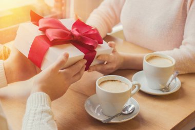 Romantik bir adamın kız arkadaşına hediye verirken sıcak bir Fransız kafesinde kahve içtiği yakın plan. Mutlu kadın erkek arkadaşından kırmızı kurdeleli hediye paketi alıyor. Tatil kutlaması konsepti