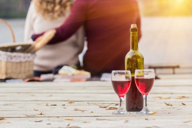 Sahilde romantik bir akşam. Yakışıklı bir adamın dışarıda romantik piknik yaparken genç kız arkadaşına sarılışının arkası. Açık havada aşık güzel bir çift. Şarap şişesi ve şarap kadehi..