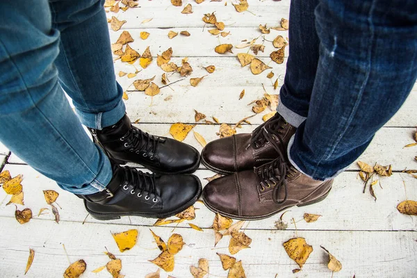 Togetherness concept. Top view couple feet in stylish boots standing together on wooden pier with yellow leaves. Young couple standing close to each other. Autumn fall. Stylish and fashionable couple