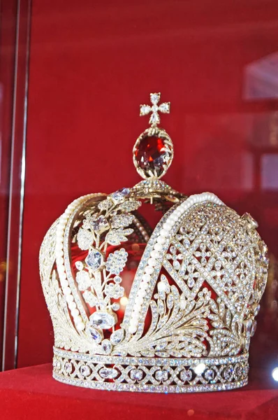Altın dan yapılmış ve çok renkli değerli taşlarla süslenmiş kraliyet tacı kırmızı kadife bir stand üzerinde duruyor