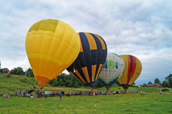 Balloons of yellow, blue, white are inflated before flying on a green glade on a summer day.