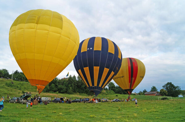 Balloons of yellow, blue, white are inflated before flying on a green glade on a summer day.