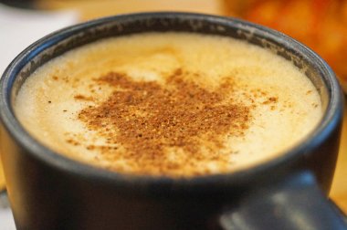 Tarçın serpilir kalın bir krema ile Cappuccino masada siyah bir fincan içine dökülür