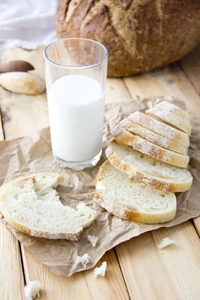 A glass of milk and cut bread on a wooden table and scattered cr — Stock Photo, Image