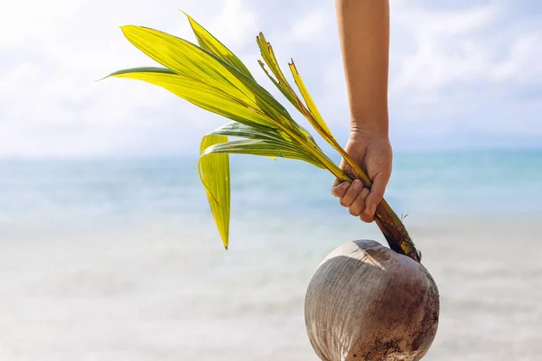 Hand van de vrouw met jonge kokosnoot op het strand — Stockfoto