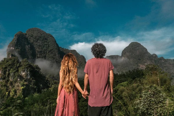 Młoda para trzyma się za ręce ciesząc się widokiem na góry — Zdjęcie stockowe